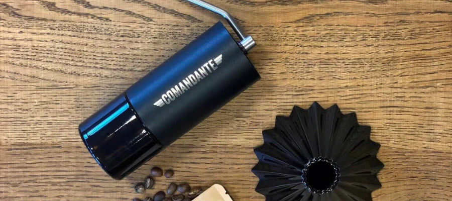Black Comandante Hand Grinder, laying alongside coffee beans | The Coffee Collective