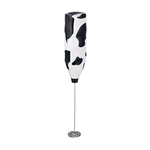 A slender, hand-held milk frother. At the top end, it has a plastic handle with a cow print design. At the opposite end, there's a whisk or frothing head made of stainless steel for aerating milk and creating froth. 